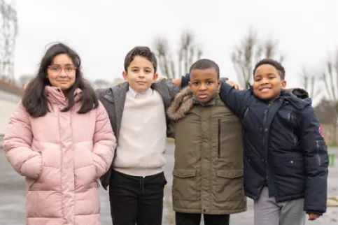 Quatre enfants, trois garçons et une fille bras dessus bras dessous regardent la caméra 